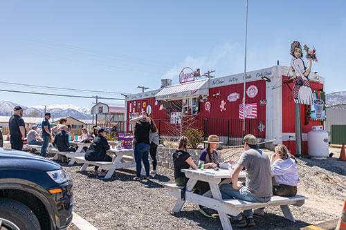 A house-trailer sized restaurant painted red, with people sitting at picnic tables outside, eating. 