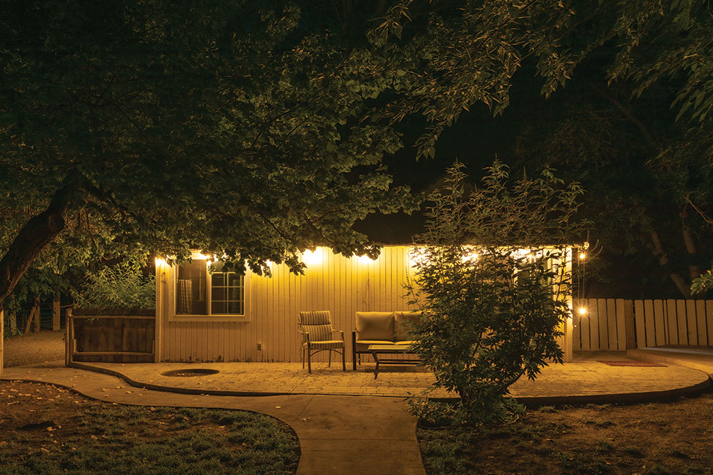 A pale yellow farmhouse at night, with strung lighting and chairs