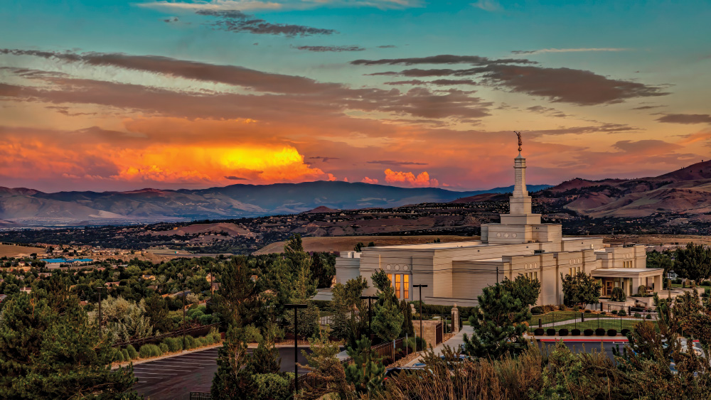Looking out over the city of Reno, the back of the Mormon/Latter Day Saints temple is in the foreground, surrounded by trees. The city is in the distance, with mountains all around, and a blazing sunset that looks like the clouds are on fire, fading to blue sky at the top.