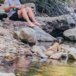 A young man sitting on rocks beside a river, fishing