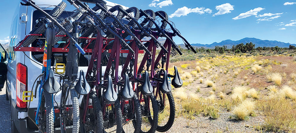 A row of mountain bikes mounted on the back of a van, with the desert in the background.