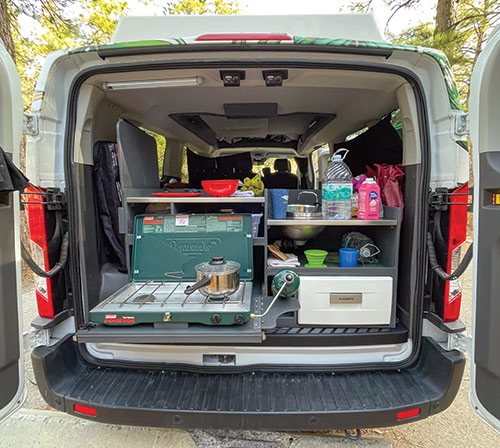 Looking into a camper van from the back, showing a cooking surface and storage options.