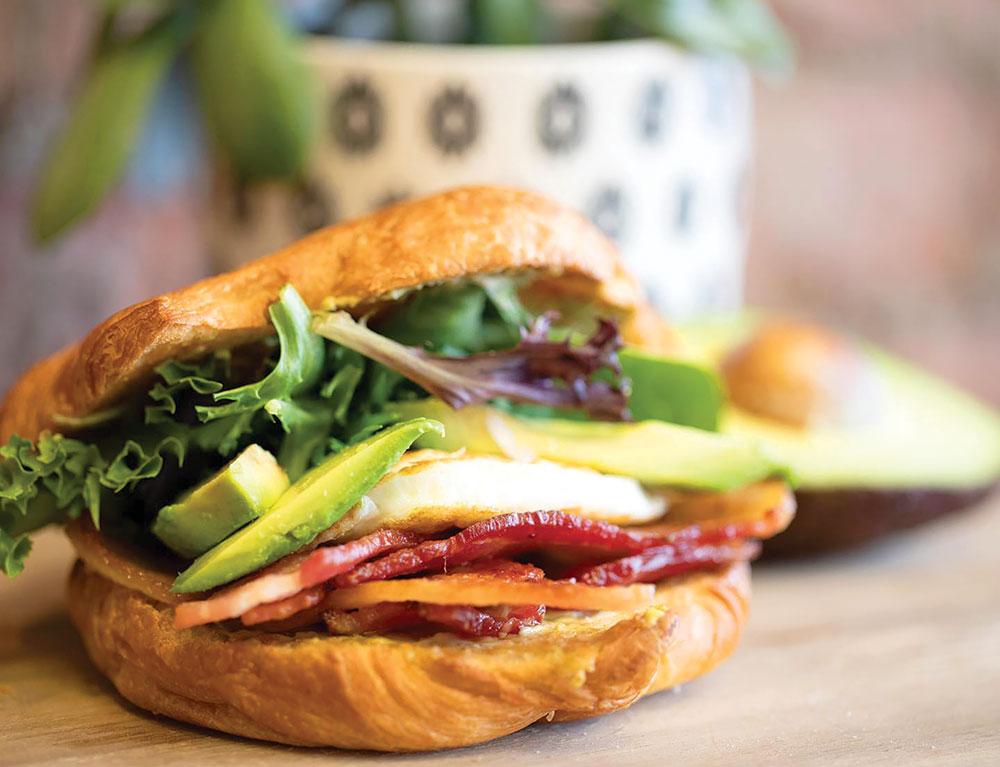 Breakfast sandwich with ham, egg, avocado, and lettuce, on a croissant