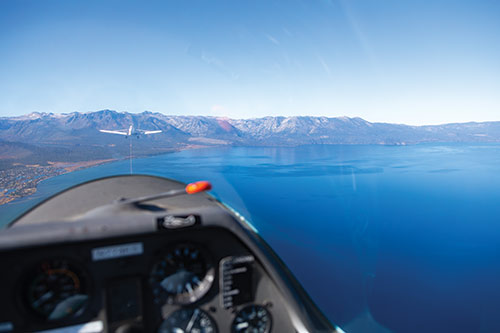 The view from a soaring plane, being towed by another. Lake Tahoe and surrounding mountains are seen below and in the distance.