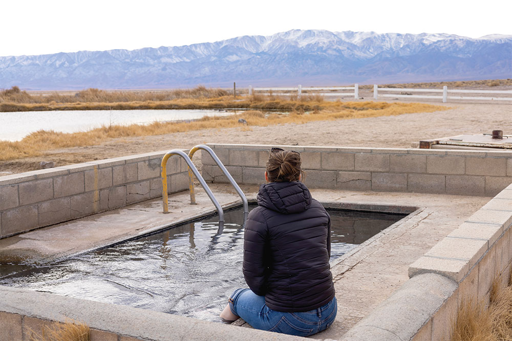 Woman sits with feet in the pool at Fish Lake Valley Hot Springs