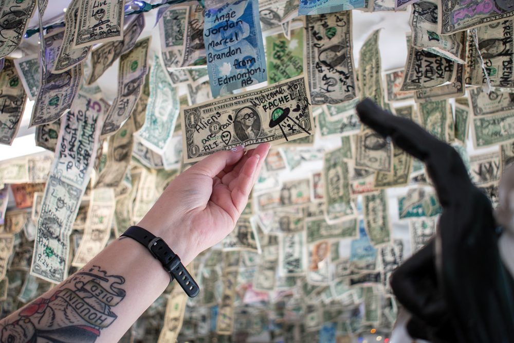 Ceiling covered in American currency with 'Aliens are real! - Ali' and 'Welcome to RACHEL! - Rachel' written on a dollar note. 