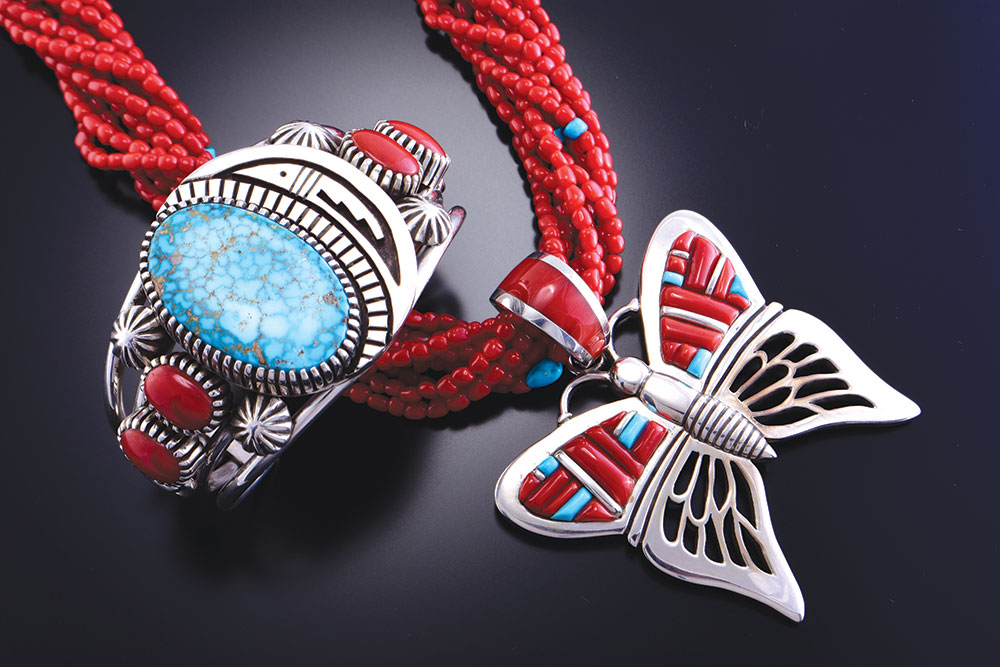 Erick Begay Native American Jewelry in Boulder City, shows beautiful silver jewelry with red and blue stones. One is a bracelet and the other is a necklace in the shape of a butterfly.