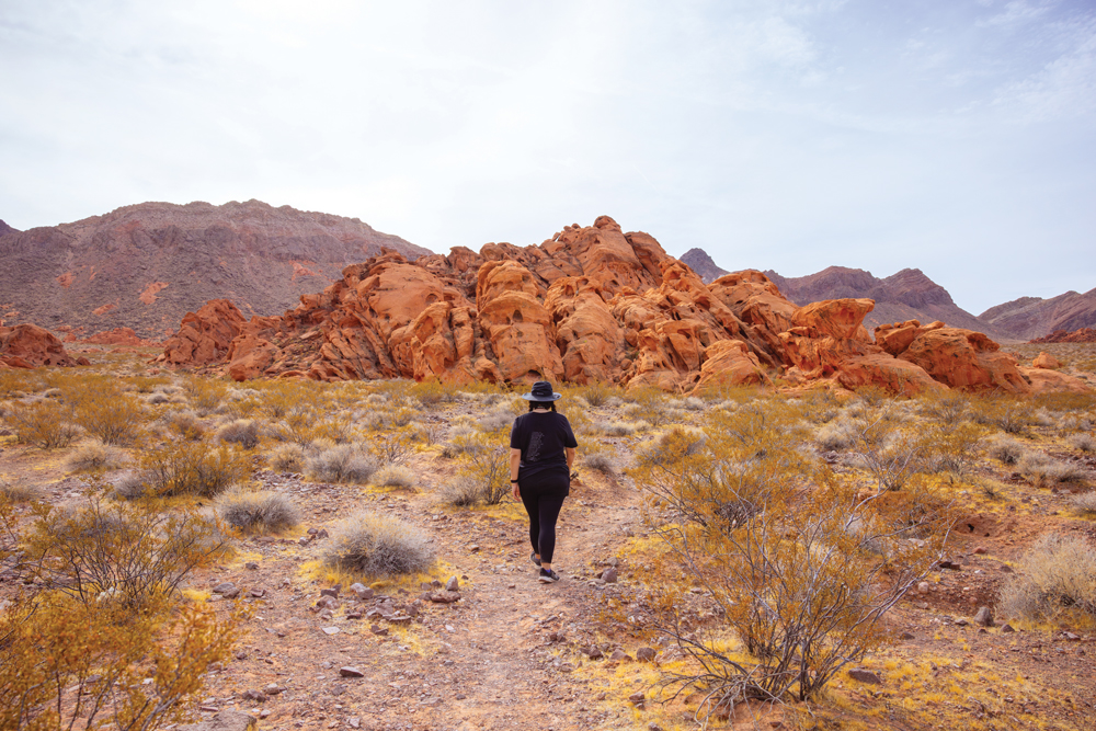 Woman walking towards red rocks along the Redstone Discovery Trail at Lake Mead National Recreation Area. 