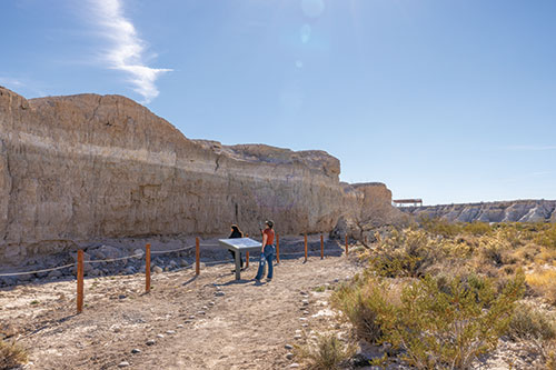 Two people read the information about a tall wall in Ice Age Fossils State Park