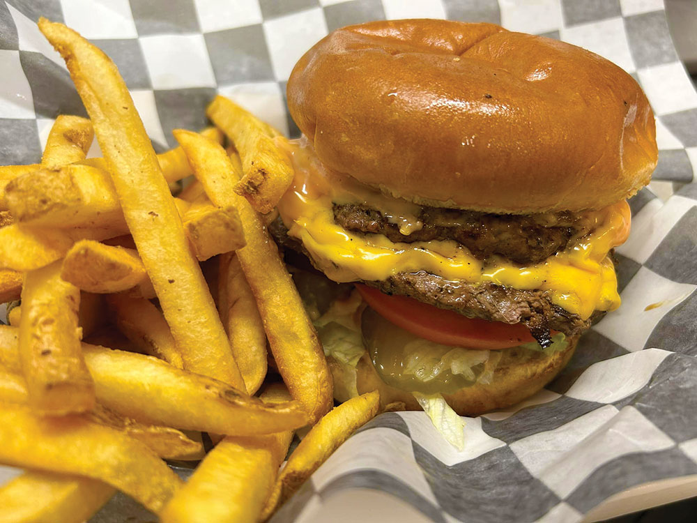 A double-patty hamburger with french fries, on gray-checkered paper.