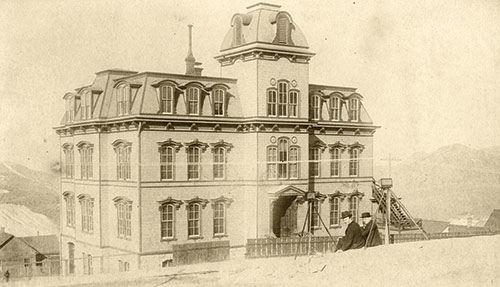 Sepia image of Fourth Ward School circa 1877, with two photographers sitting on the wall in front of it.