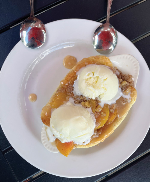 Apple cobbler on a white plate, with melting vanilla ice cream on top, and two spoons.