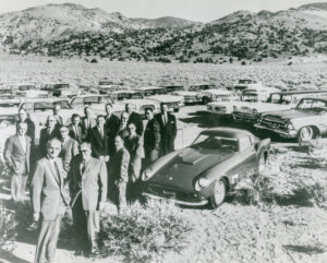 Bill Harrah standing with a group of men with several cars behind them.