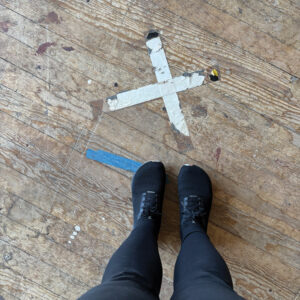 Feet standing next to an 'x' taped on the floor of the Washoe Club.