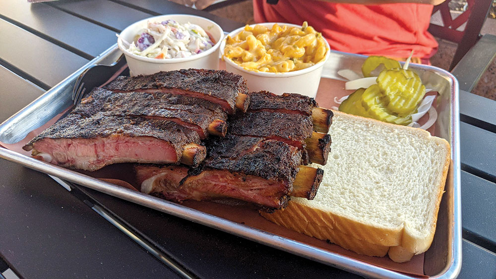 A platter of ribs, coleslaw, macaroni and cheese, bread, and pickles