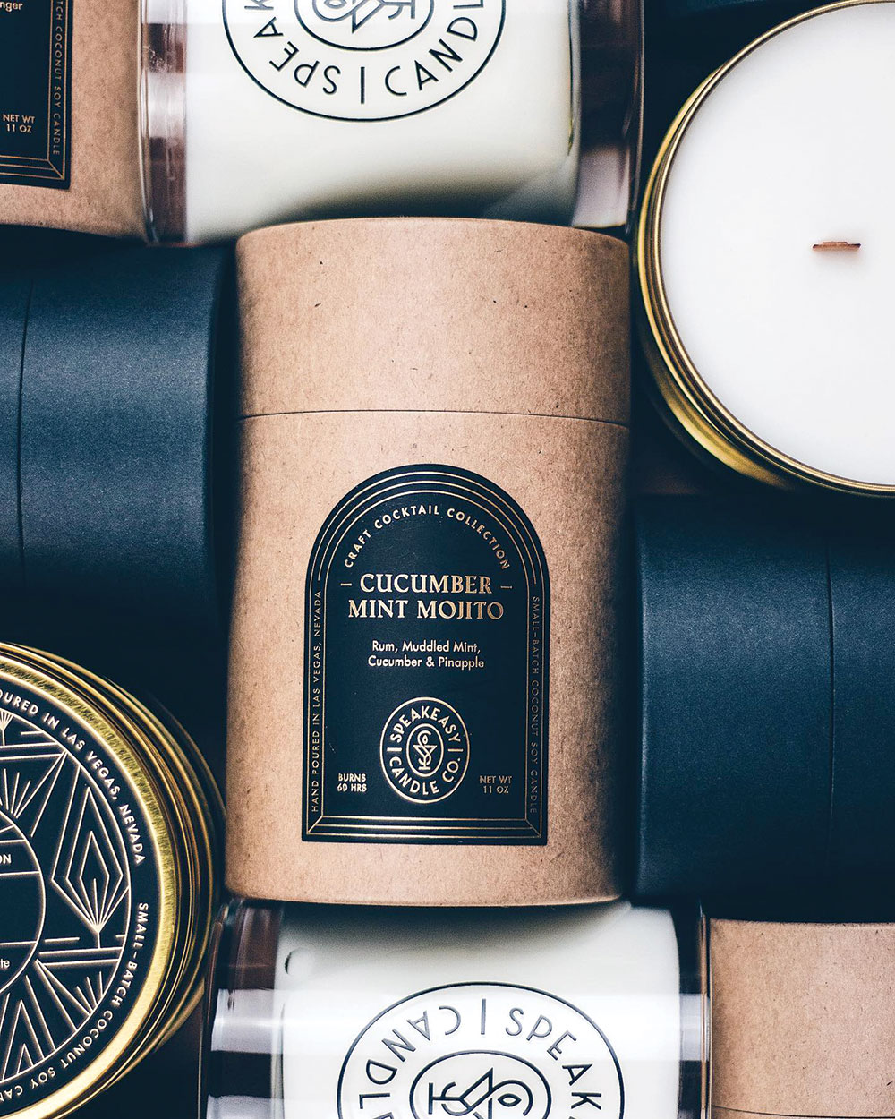 Speakeasy Candle Company in Las Vegas, image shows a close-up of candles in cardboard containers and also out by themselves. The center is in brown cardboard and indicates it is Cucumber Mint Mojito scented.