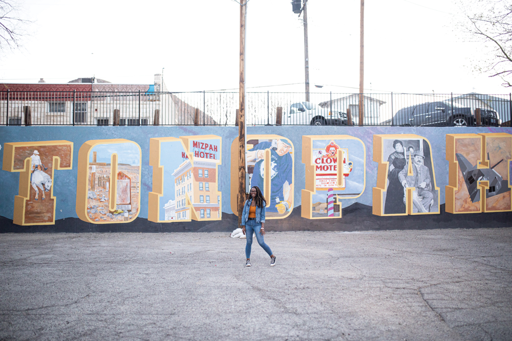 Woman standing in front of a mural spelling out Tonopah with pictures in the letters. 