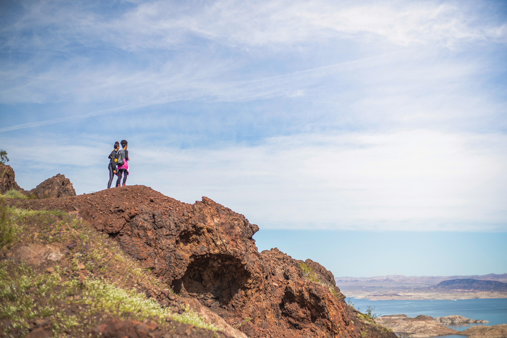 Two girls standing on top of a rocky outcrop, looking over Lake Mead.