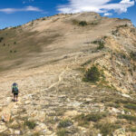 A hiker on an uphill trail on a tall mountain