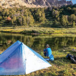 A man sitting beside a tent and an alpine lake